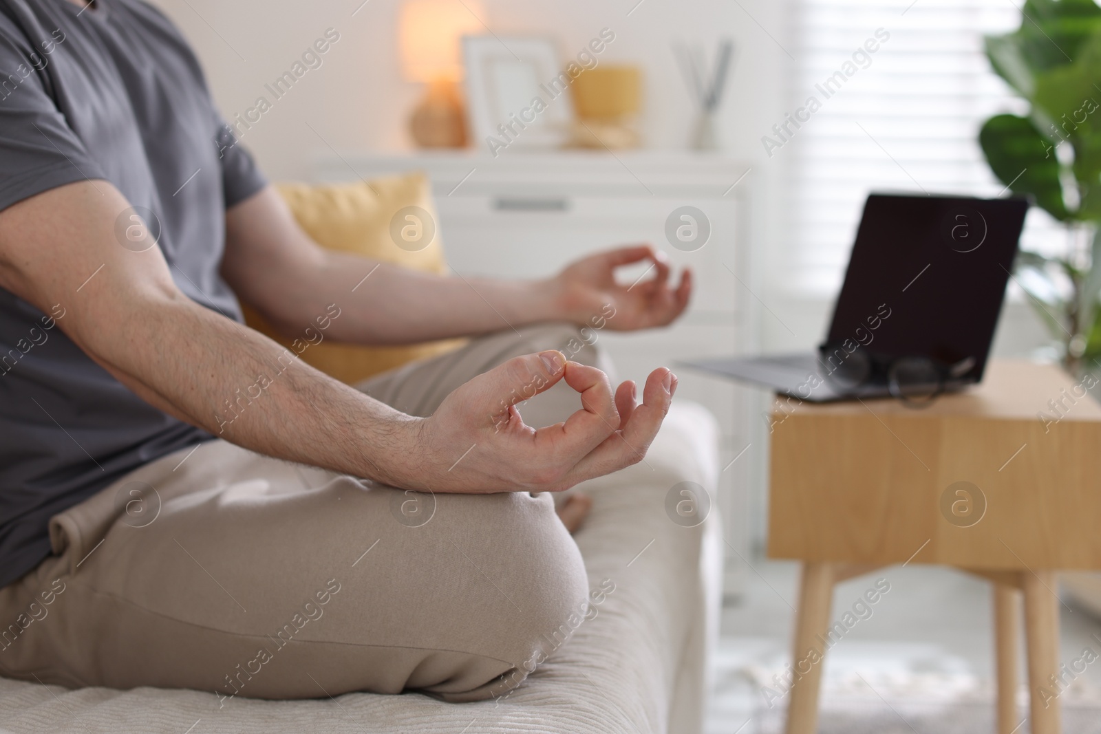 Photo of Man meditating near laptop on sofa at home, selective focus