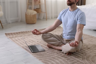 Photo of Man meditating near laptop on floor at home, closeup