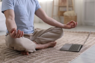 Photo of Man meditating near laptop on floor at home, closeup