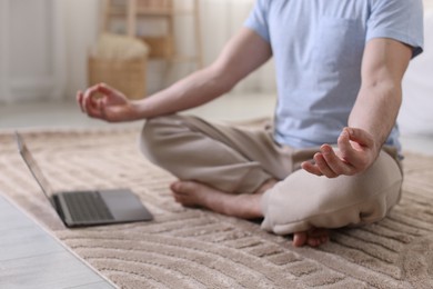 Photo of Man meditating near laptop on floor at home, closeup