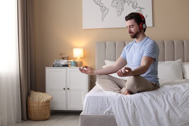 Photo of Man in headphones meditating on bed at home