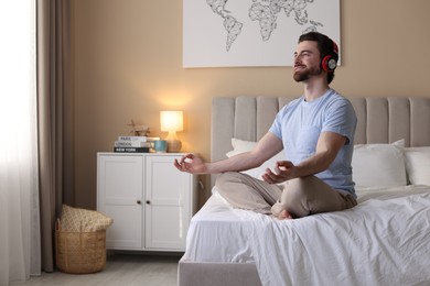 Photo of Smiling man in headphones meditating on bed at home