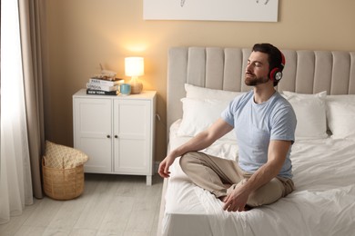 Photo of Man in headphones meditating on bed at home