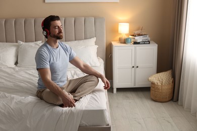 Photo of Man in headphones meditating on bed at home