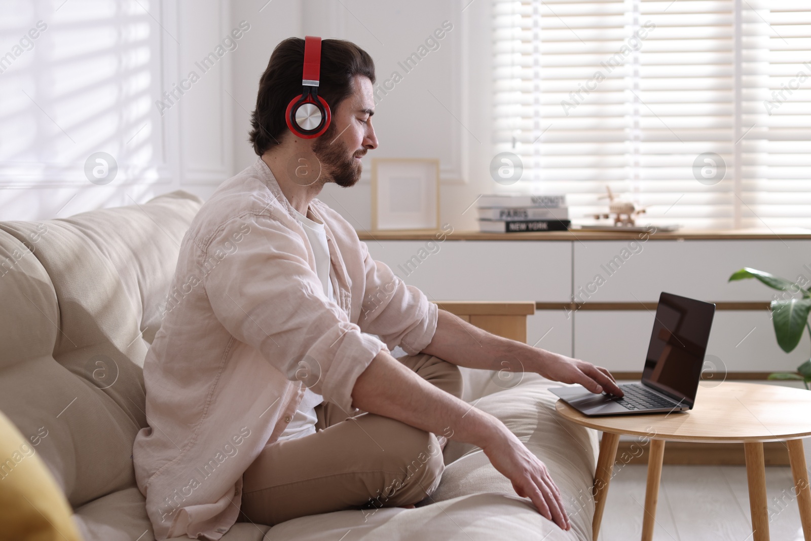 Photo of Meditation. Man in headphones watching video tutorial by laptop on sofa at home