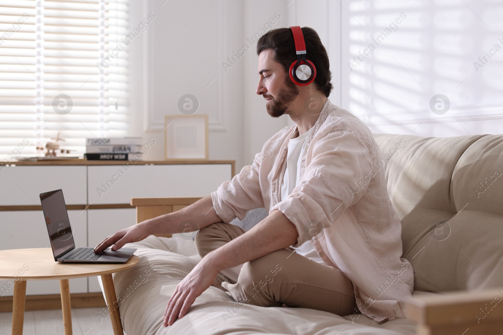 Photo of Meditation. Man in headphones watching video tutorial by laptop on sofa at home