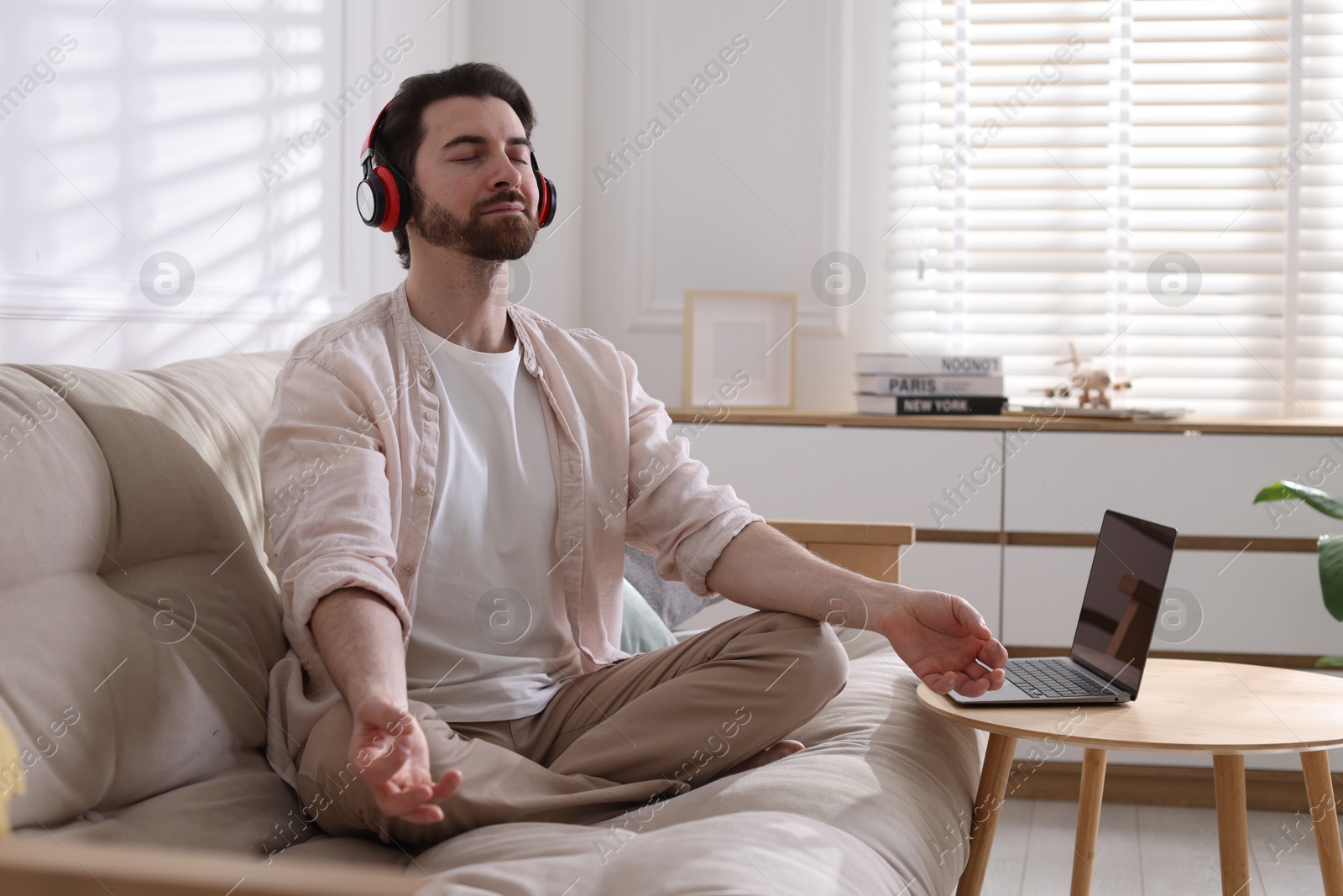 Photo of Man meditating near laptop on sofa at home