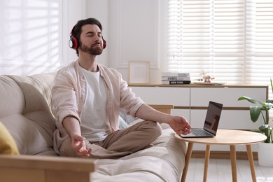 Photo of Man meditating near laptop on sofa at home