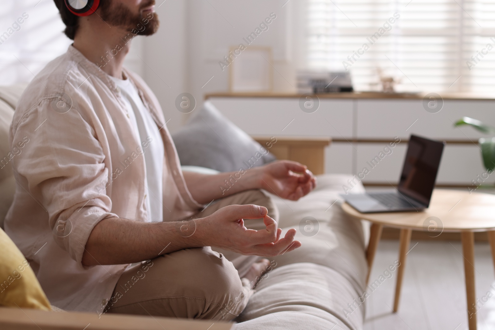 Photo of Man meditating on sofa and laptop at home, selective focus