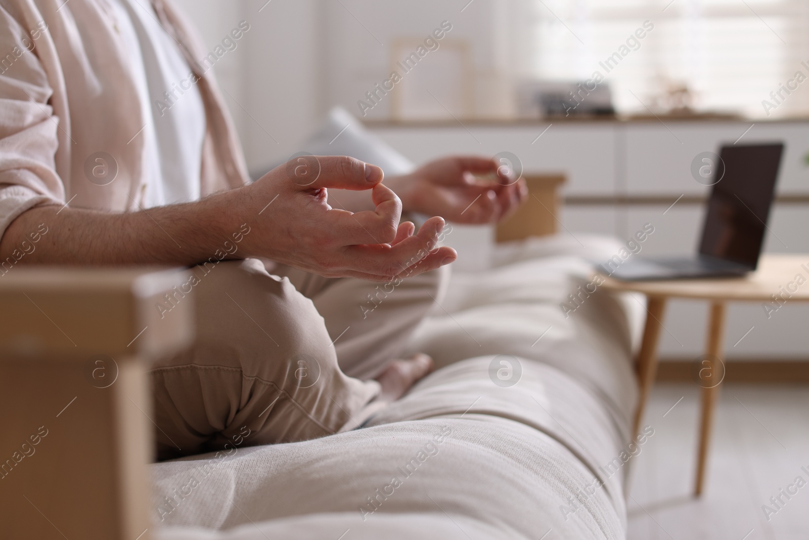 Photo of Man meditating on sofa and laptop at home, selective focus