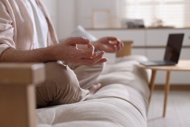 Photo of Man meditating on sofa and laptop at home, selective focus