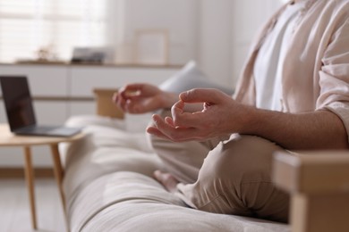 Photo of Man meditating on sofa and laptop at home, selective focus