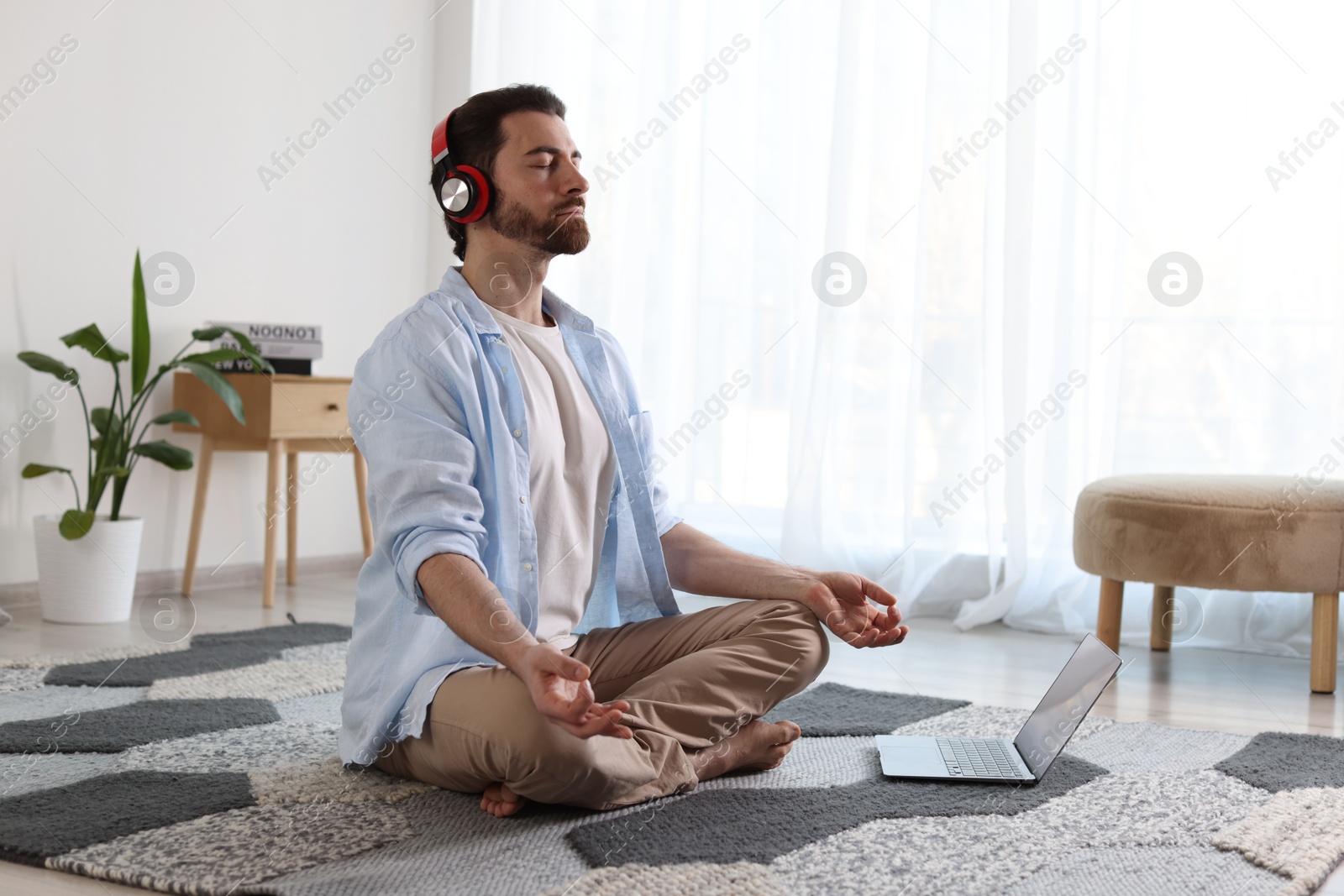 Photo of Man in headphones meditating near laptop on floor at home