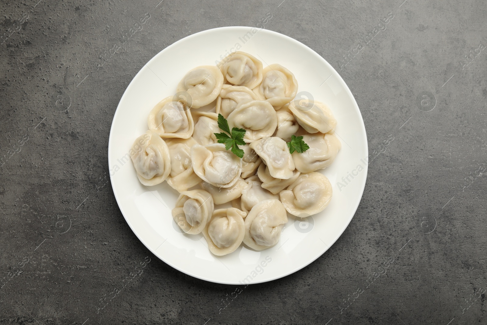 Photo of Delicious dumplings with fresh parsley on grey table, top view