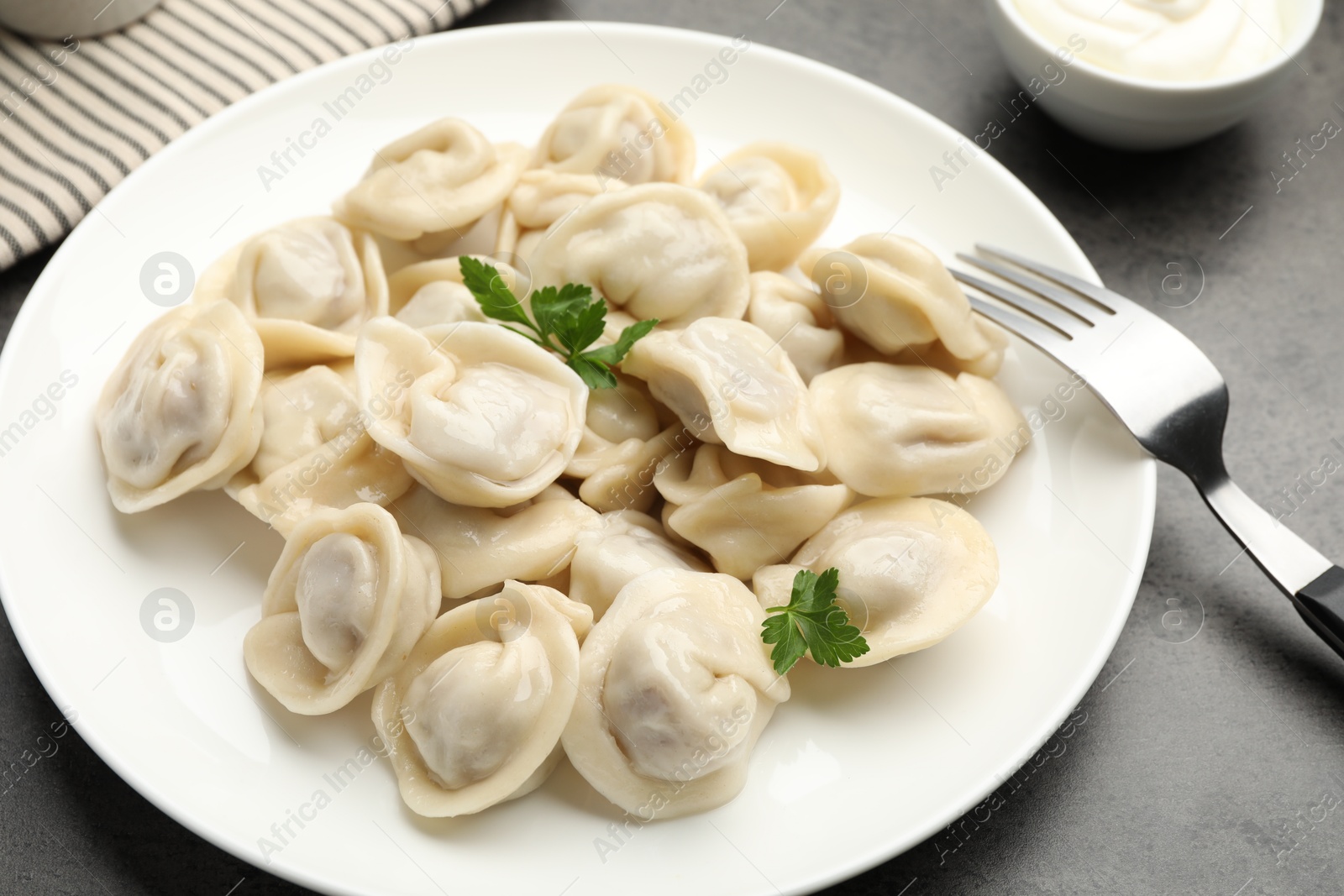 Photo of Delicious dumplings with fresh parsley served on grey table, closeup