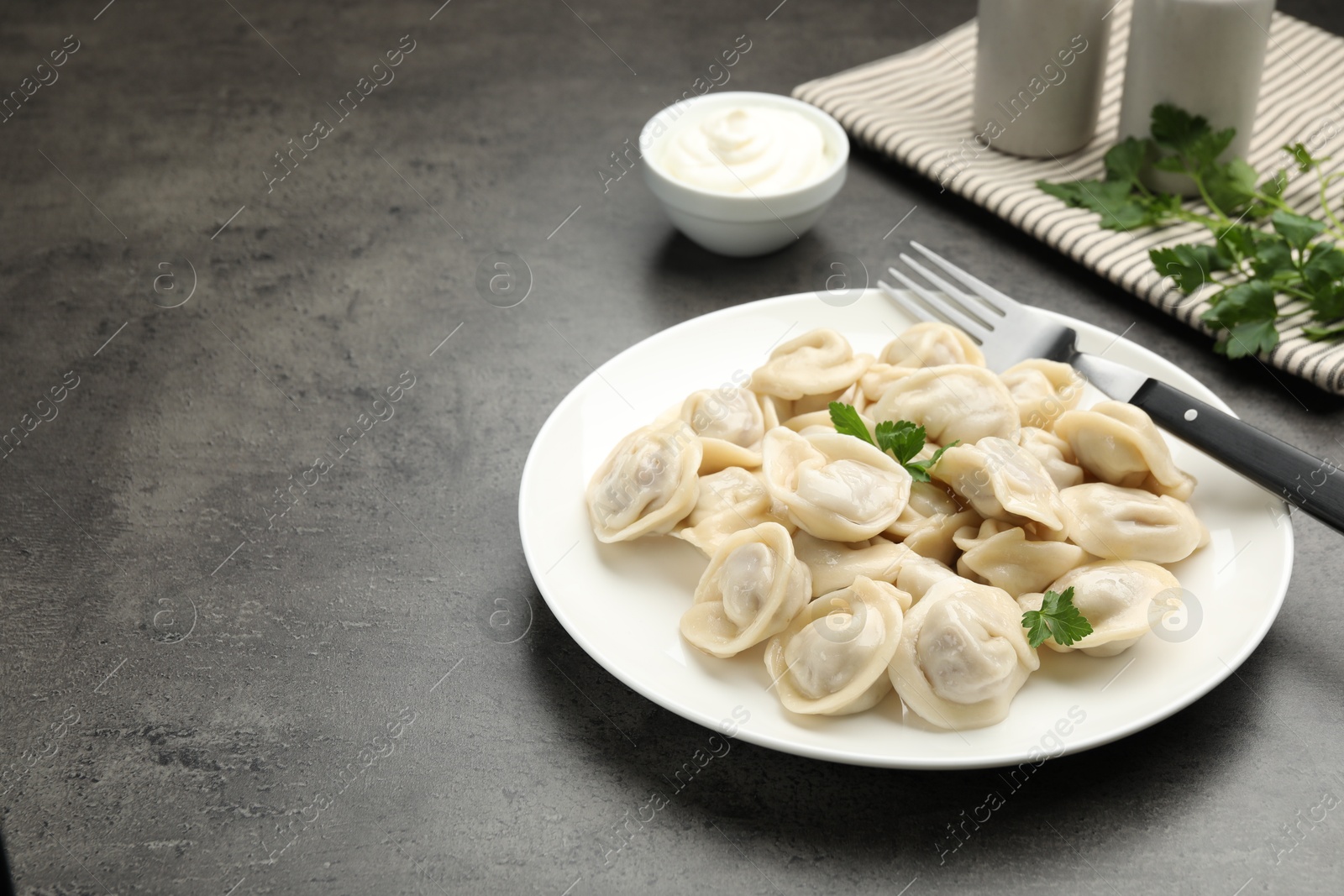 Photo of Delicious dumplings with fresh parsley served on grey table, space for text