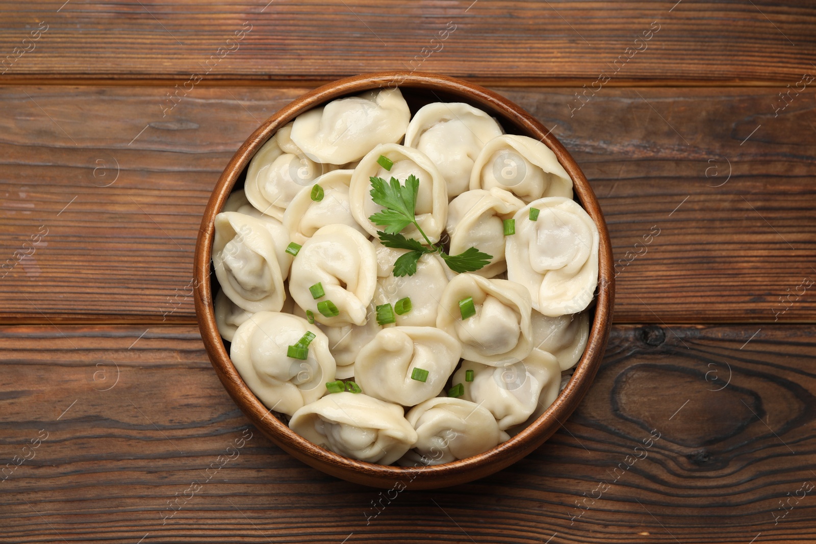 Photo of Delicious dumplings with fresh green onion and parsley on wooden table, top view