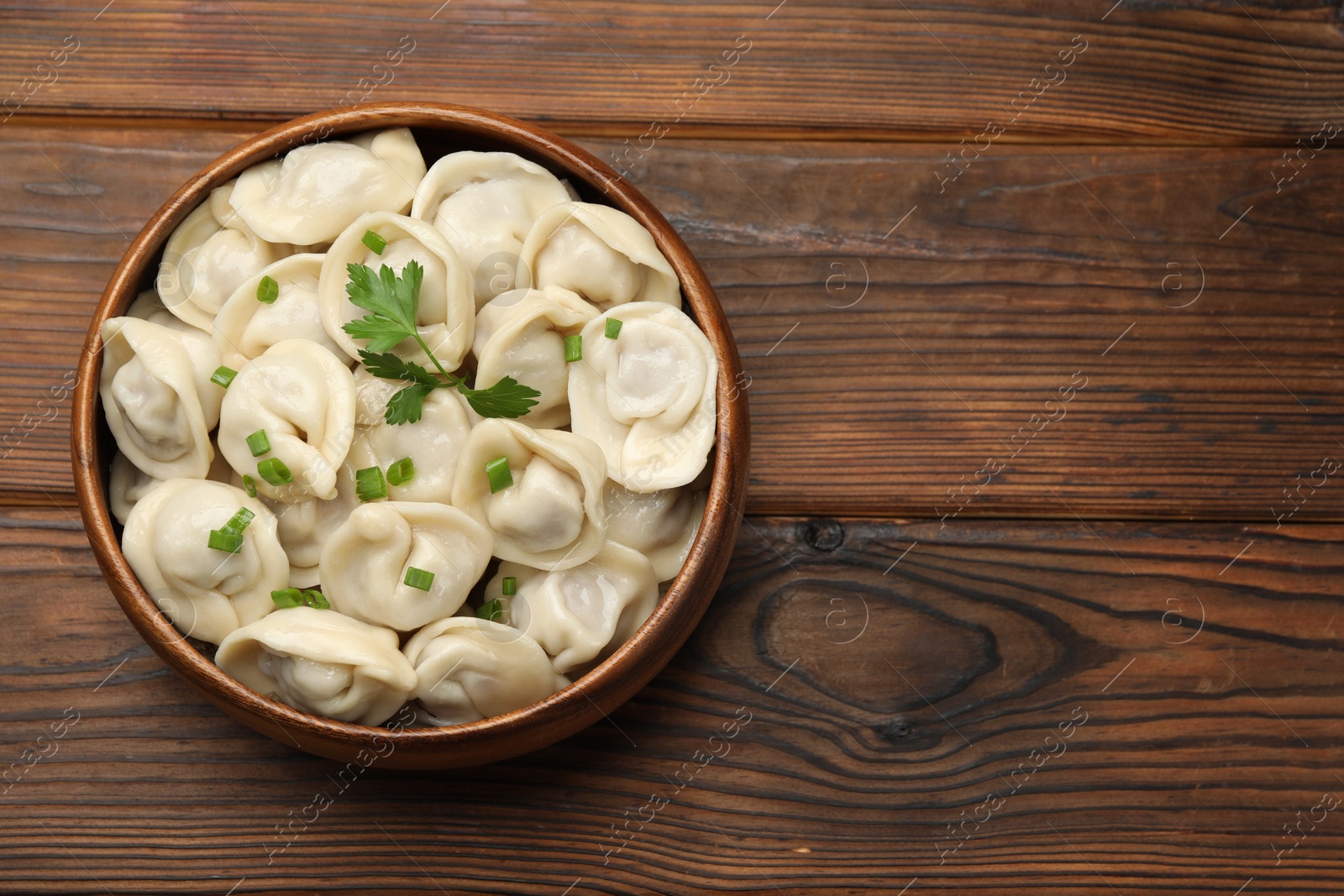 Photo of Delicious dumplings with fresh green onion and parsley on wooden table, top view. Space for text