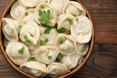 Photo of Delicious dumplings with fresh green onion and parsley on wooden table, top view