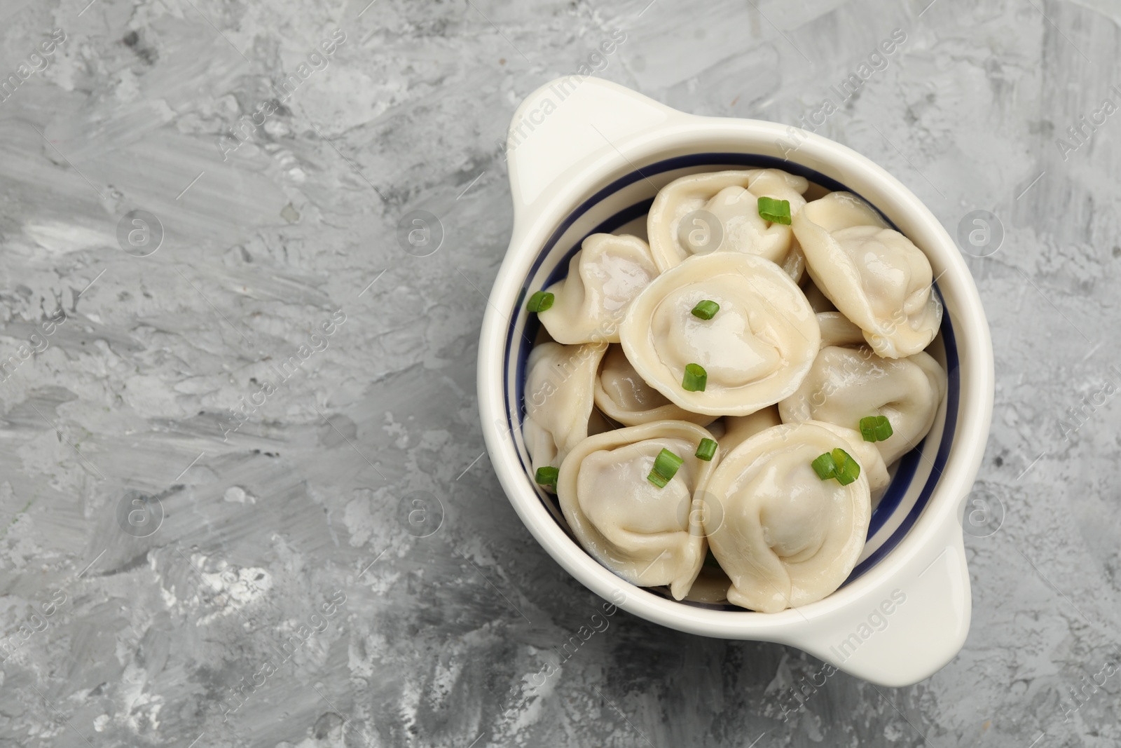 Photo of Delicious dumplings (pelmeni) with green onion in bowl on grey table, top view. Space for text