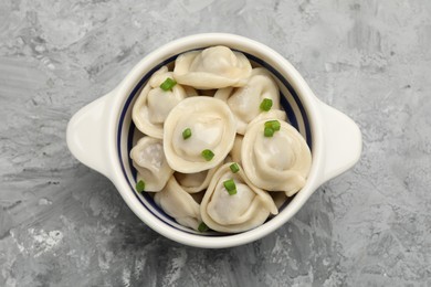 Photo of Delicious dumplings (pelmeni) with green onion in bowl on grey table, top view