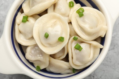 Photo of Delicious dumplings (pelmeni) with green onion in bowl on grey table, top view