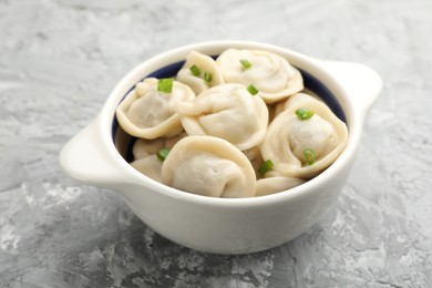 Photo of Delicious dumplings (pelmeni) with green onion in bowl on grey table, closeup