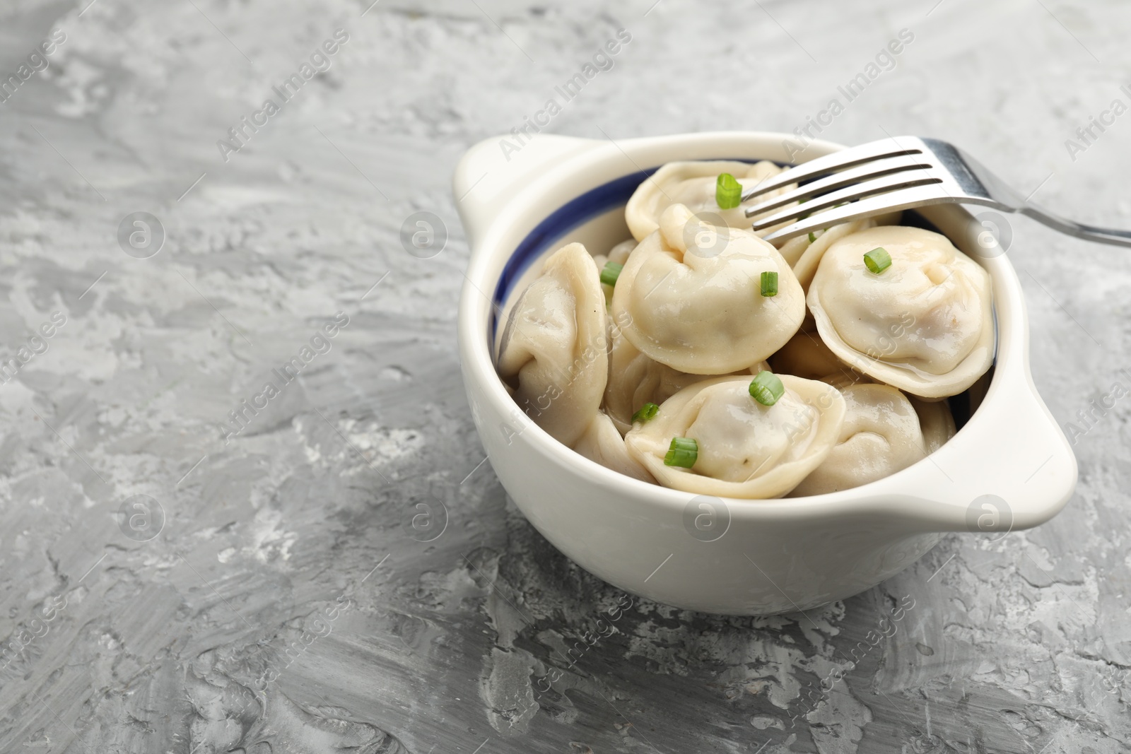 Photo of Delicious dumplings (pelmeni) with green onion in bowl and fork on grey table, space for text