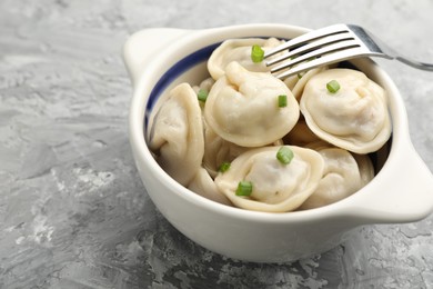 Photo of Delicious dumplings (pelmeni) with green onion in bowl and fork on grey table, closeup