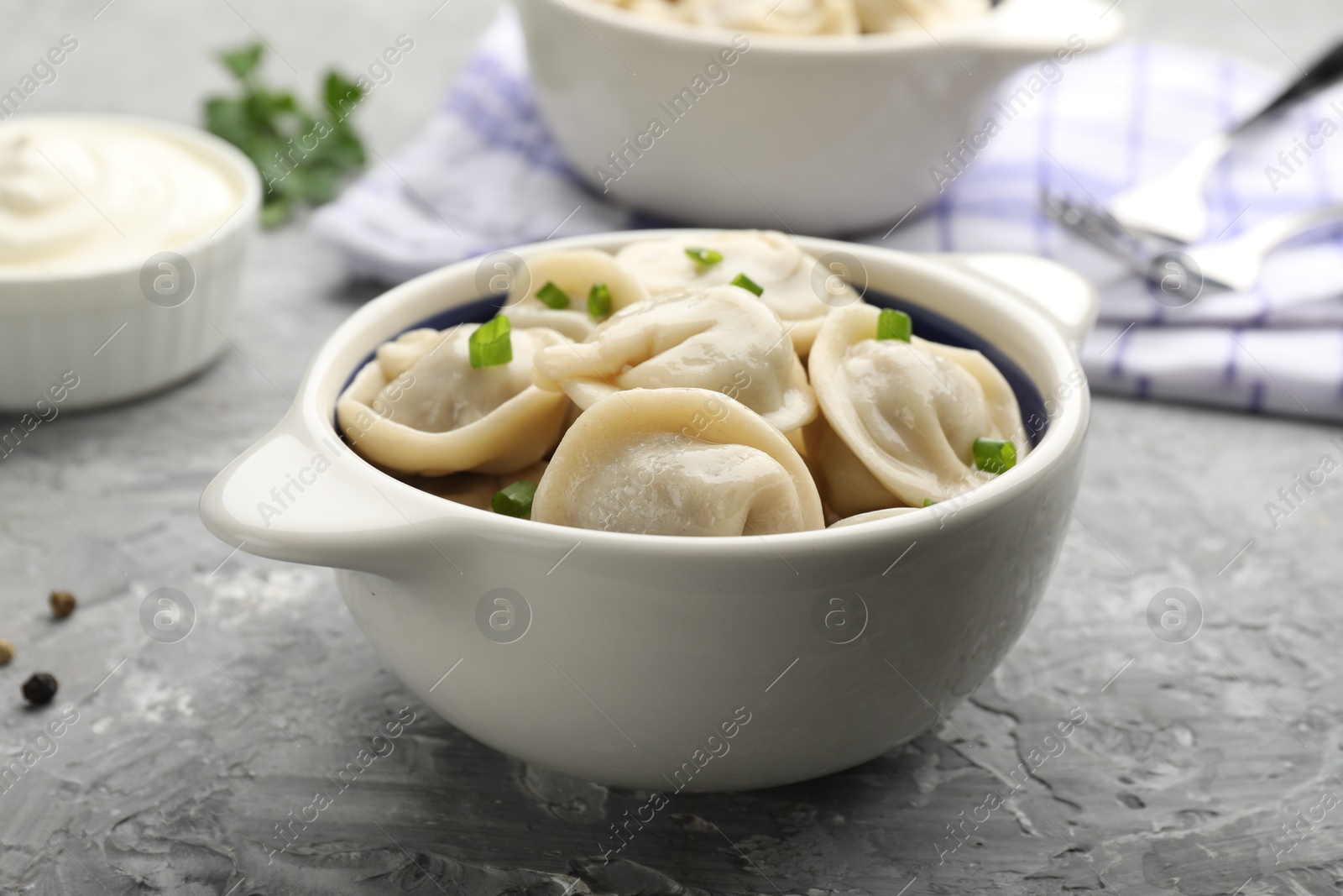 Photo of Delicious dumplings (pelmeni) with green onion in bowl on grey table, closeup