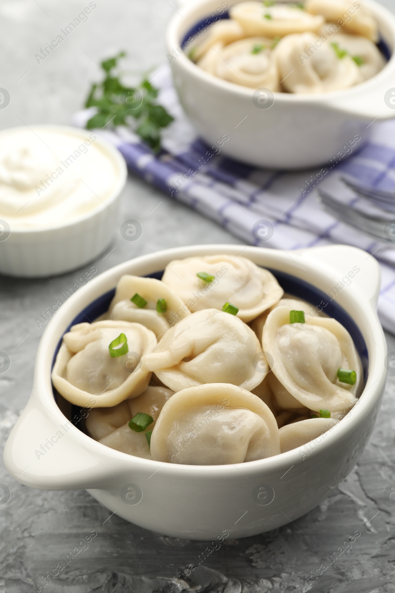 Photo of Delicious dumplings (pelmeni) with green onion in bowl on grey table, closeup