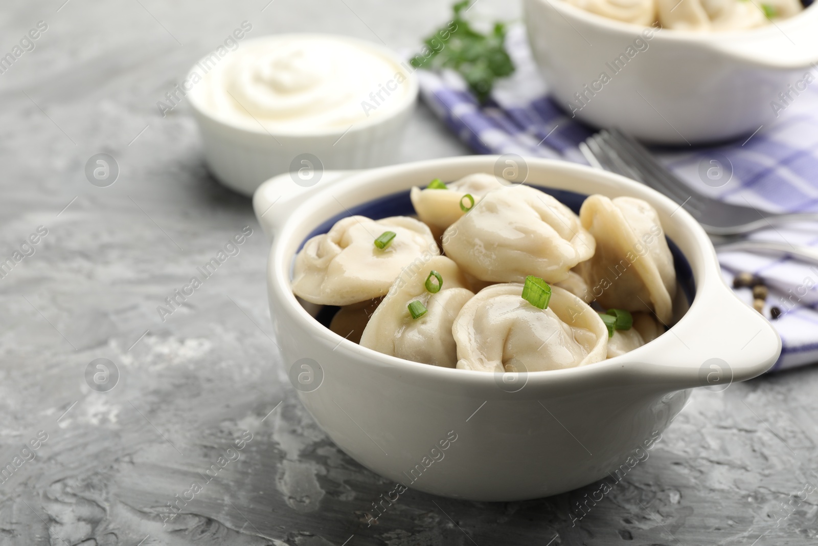 Photo of Delicious dumplings (pelmeni) with green onion in bowl on grey table, closeup