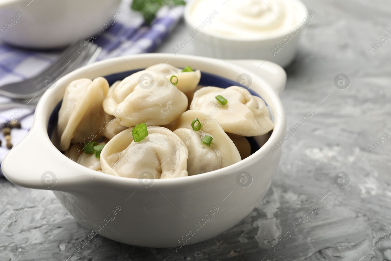 Photo of Delicious dumplings (pelmeni) with green onion in bowl on grey table, closeup