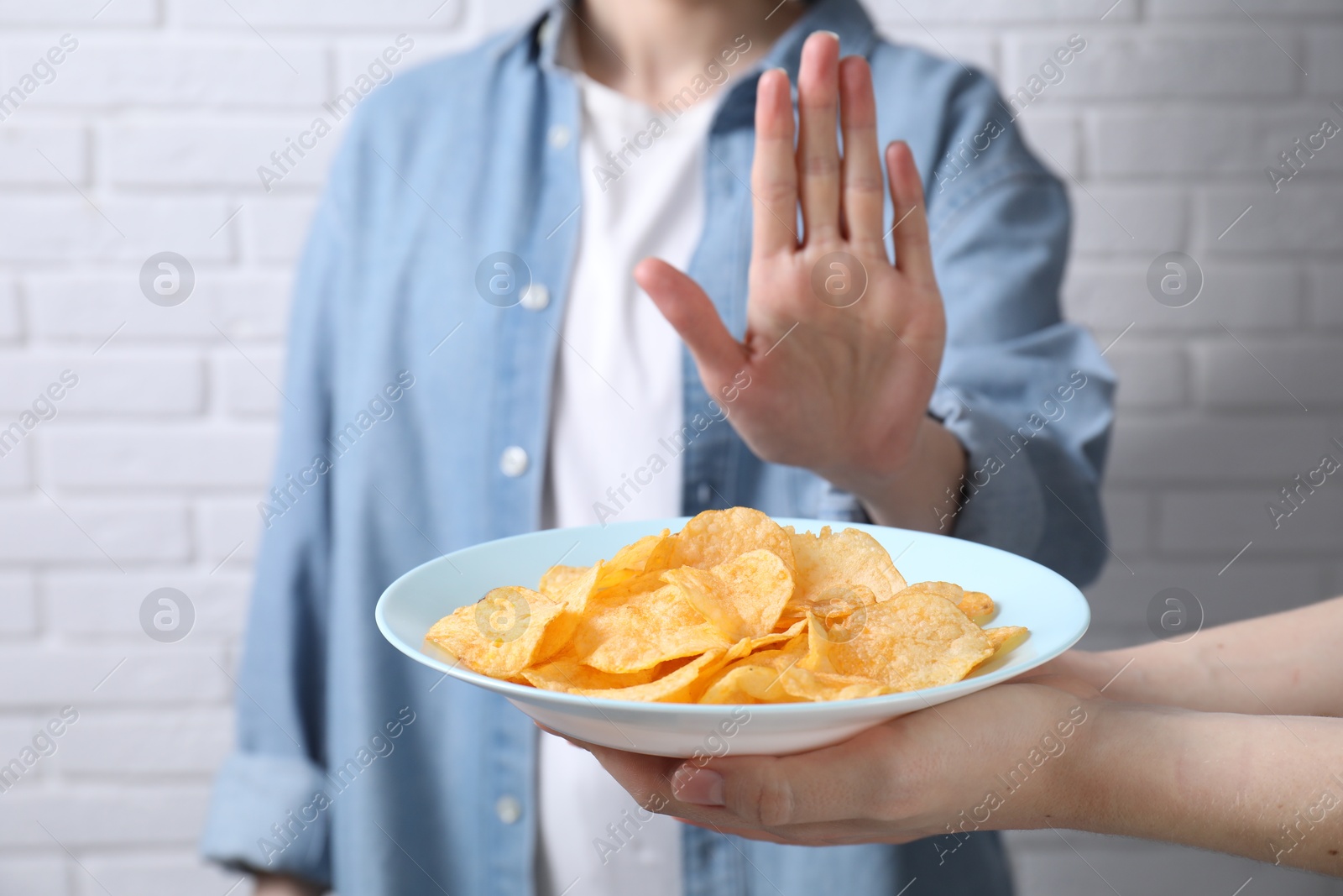 Photo of Woman refusing chips near white brick wall, selective focus. Food allergy concept