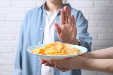 Photo of Woman refusing chips near white brick wall, selective focus. Food allergy concept