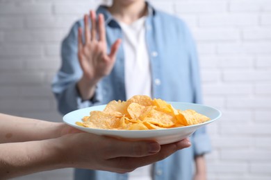 Photo of Woman refusing chips near white brick wall, selective focus. Food allergy concept