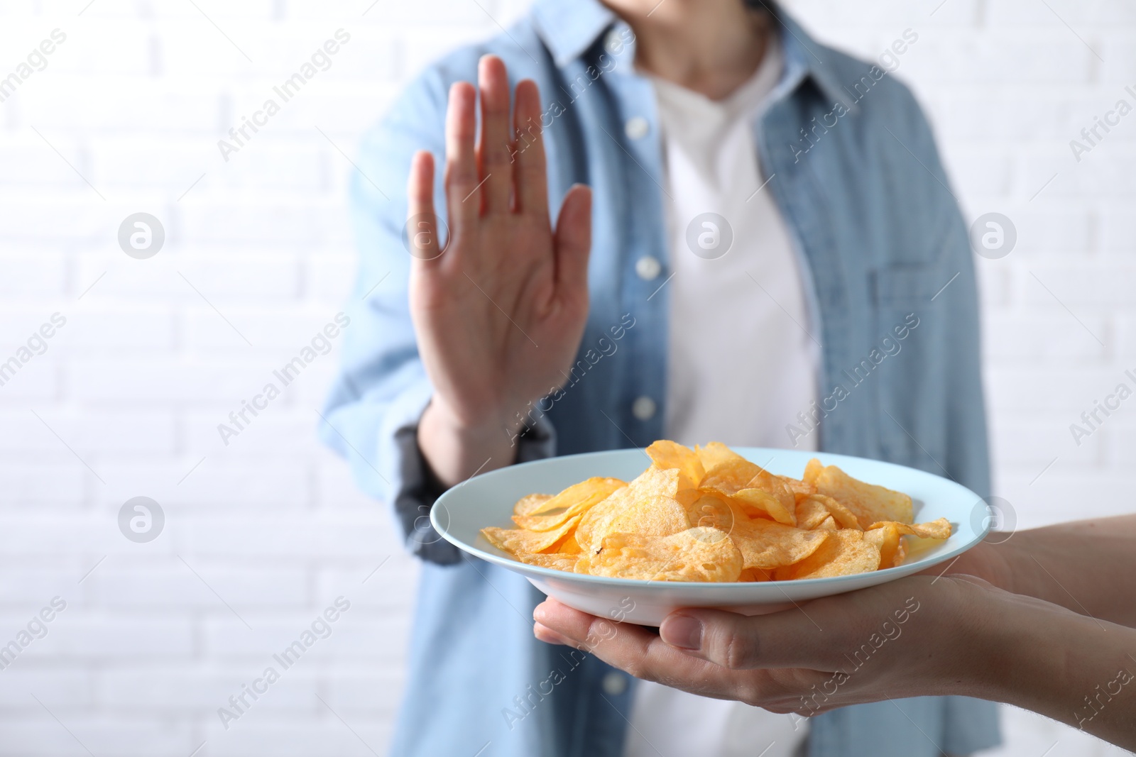 Photo of Woman refusing chips near white brick wall, selective focus. Food allergy concept