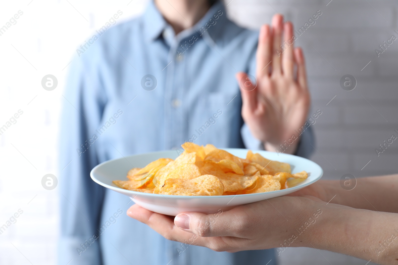 Photo of Woman refusing chips near white brick wall, selective focus. Food allergy concept