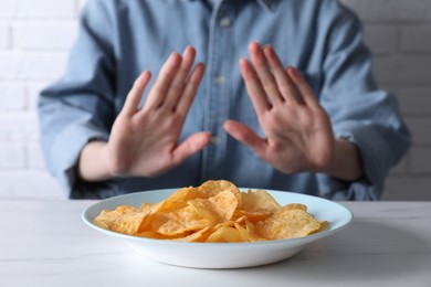 Photo of Woman refusing to eat chips at white marble table, selective focus. Food allergy concept