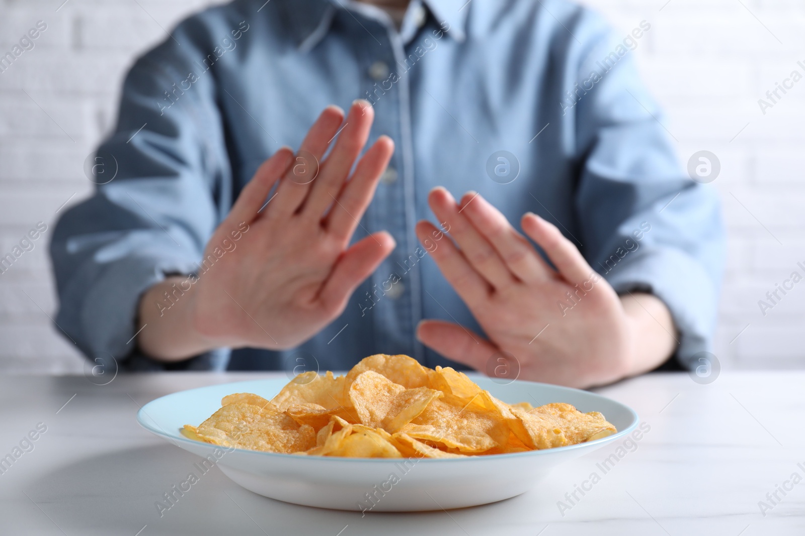 Photo of Woman refusing to eat chips at white marble table, selective focus. Food allergy concept