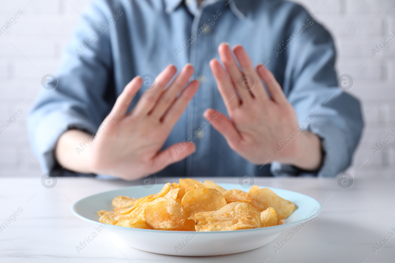 Photo of Woman refusing to eat chips at white marble table, selective focus. Food allergy concept