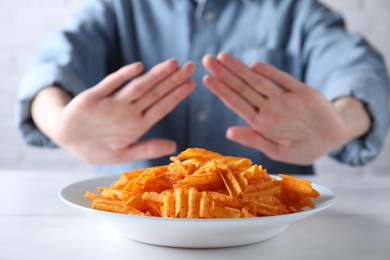 Photo of Woman refusing to eat chips at white table, selective focus. Food allergy concept