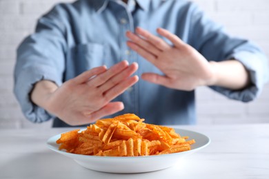 Photo of Woman refusing to eat chips at white table, selective focus. Food allergy concept