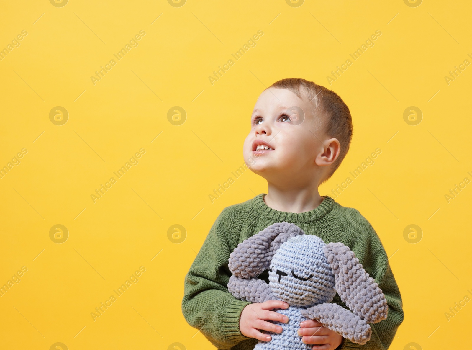 Photo of Cute little boy with toy bunny on yellow background. Space for text