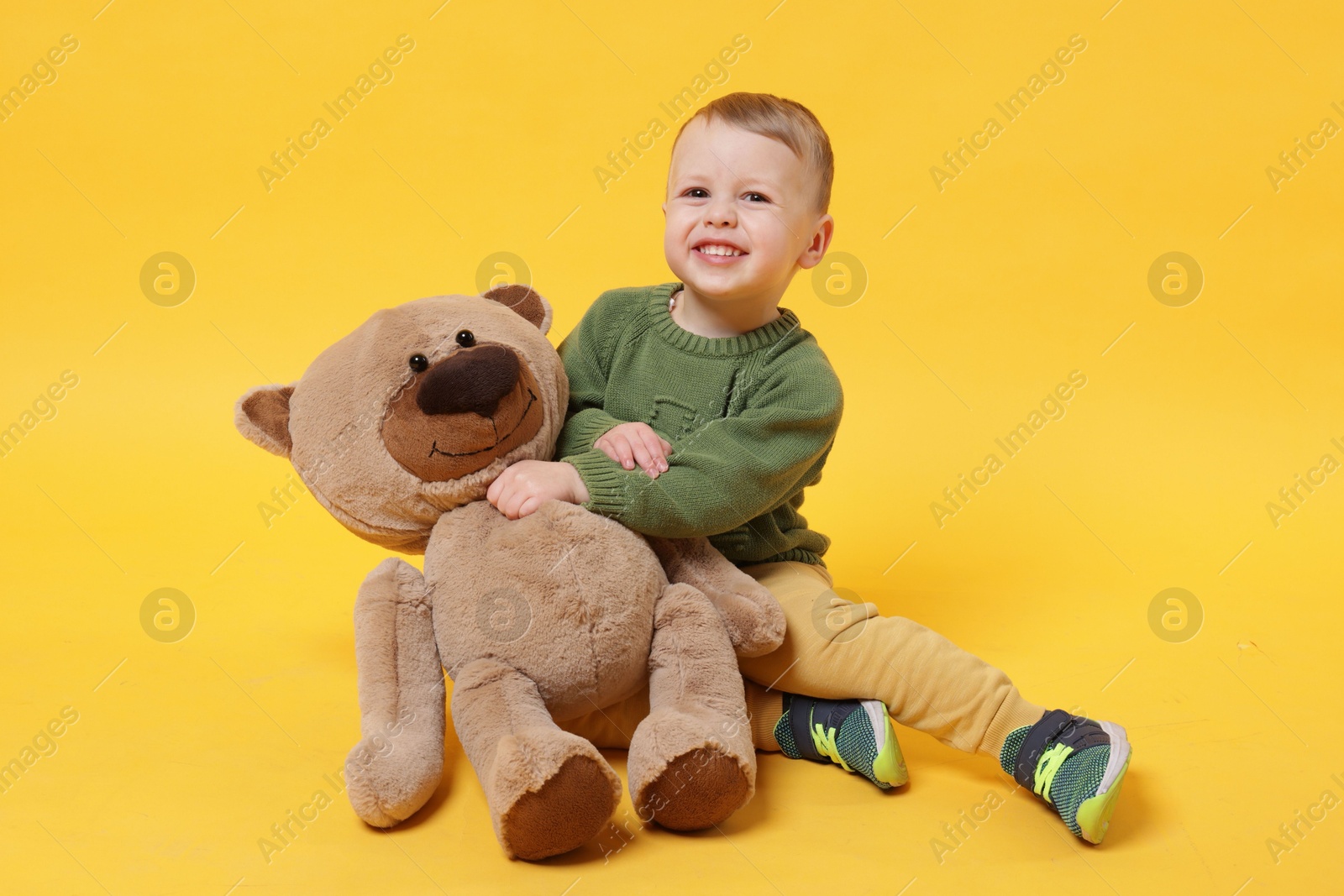 Photo of Cute little boy with toy bear on yellow background