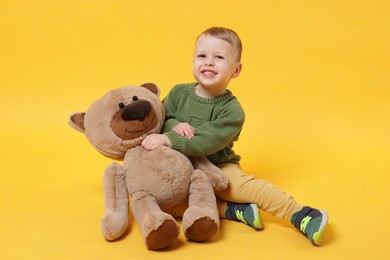 Photo of Cute little boy with toy bear on yellow background