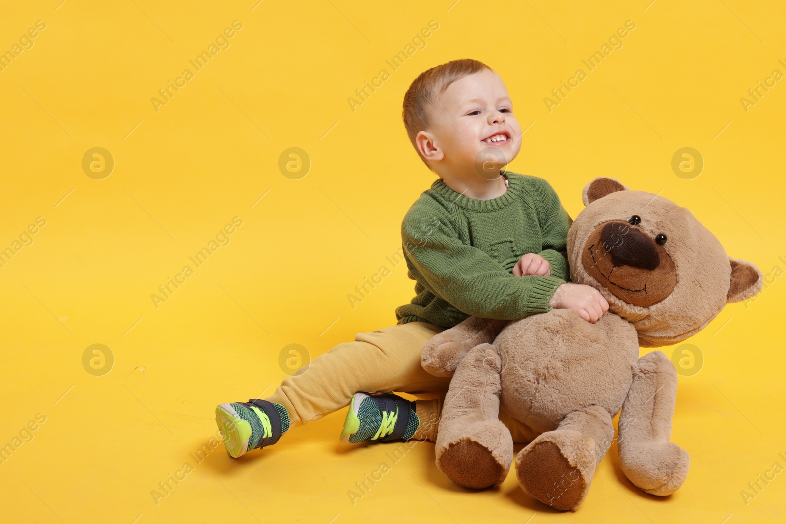 Photo of Cute little boy with toy bear on yellow background. Space for text