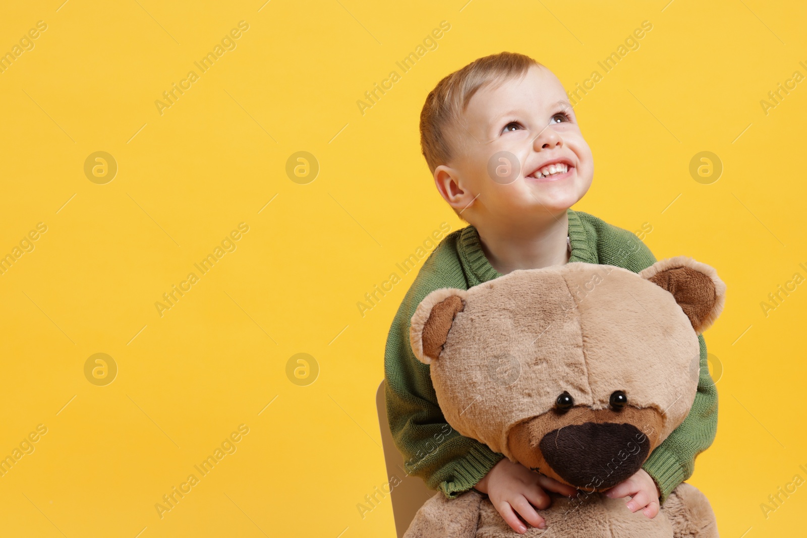 Photo of Cute little boy with toy bear on yellow background. Space for text