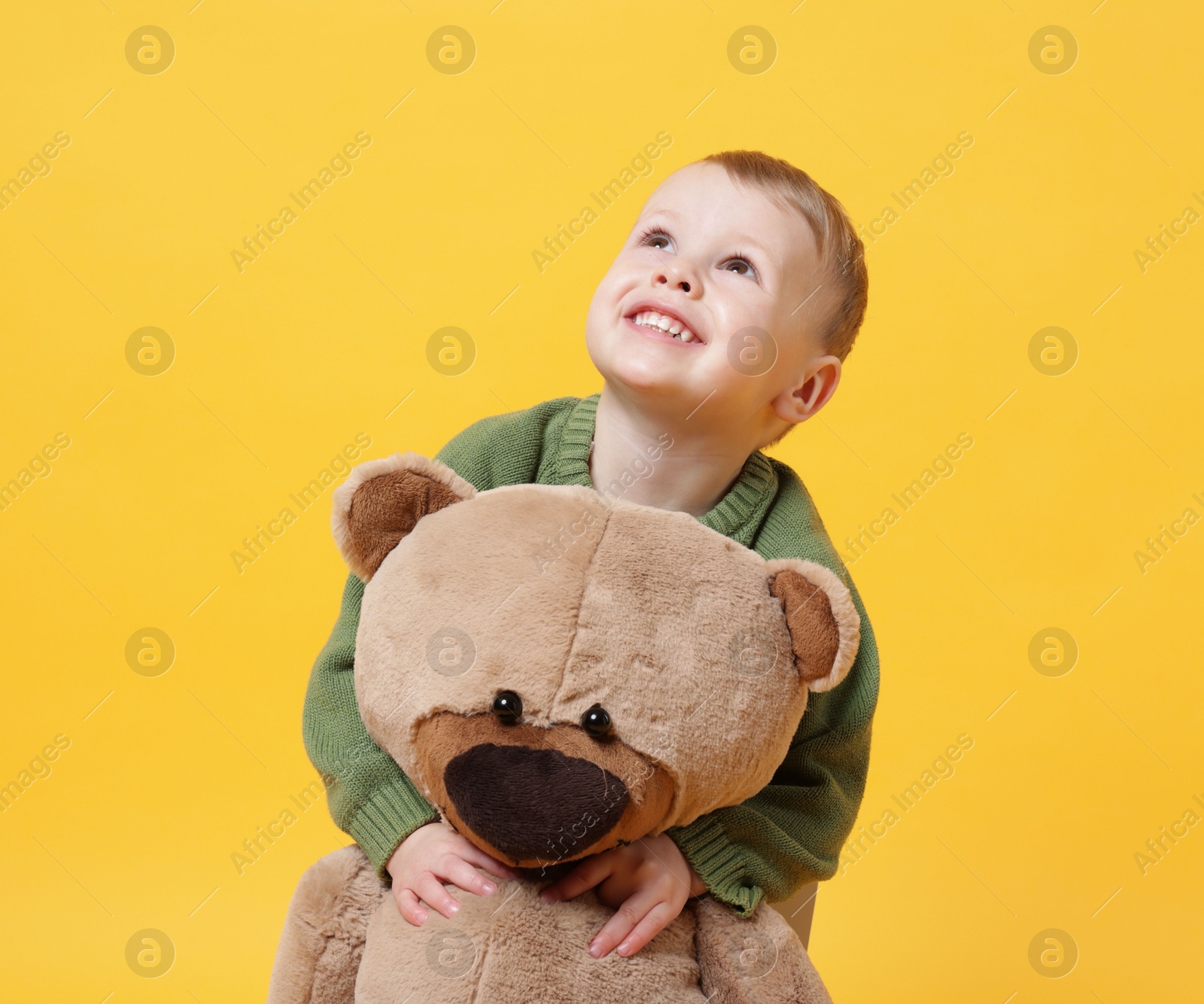 Photo of Cute little boy with toy bear on yellow background