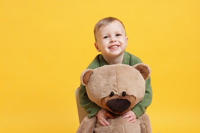 Photo of Cute little boy with toy bear on yellow background. Space for text